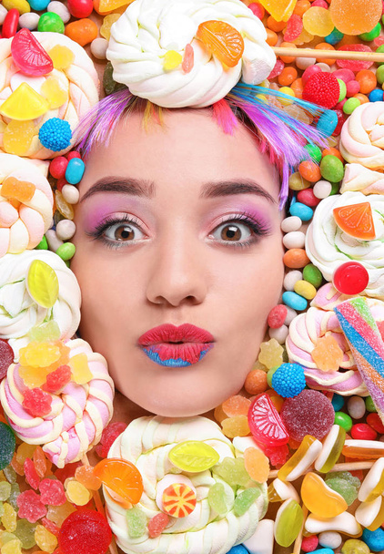 gezicht van mooie jonge vrouw met creatieve make-up omgeven door verschillende snoepjes - Foto, afbeelding