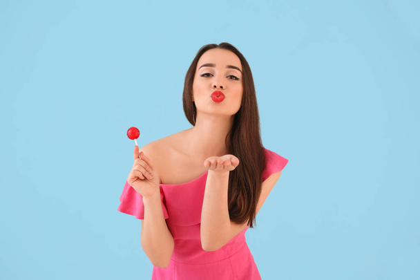 Attractive young woman with lollipop blowing kiss on color background - Foto, Imagen