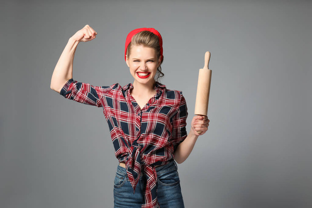 Strong young woman with rolling pin on grey background - Fotoğraf, Görsel