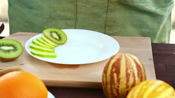 A woman puts pieces of kiwi, which is on a cutting board, on a plate. - Video, Çekim