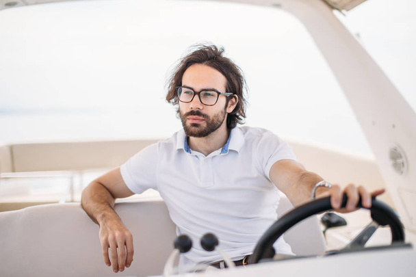 Young handsome bearded sailor man driving his motor boat - 写真・画像