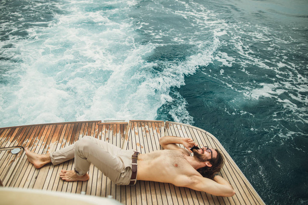 Człowiek relaksujący się pod słońcem, leżący na łodzi na morzu. Luksusowe wakacje na jachcie na wyspach. - Zdjęcie, obraz