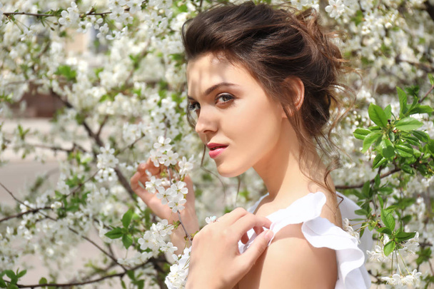 Mooie jonge vrouw in de buurt van bloeiende boom op de lente - Foto, afbeelding