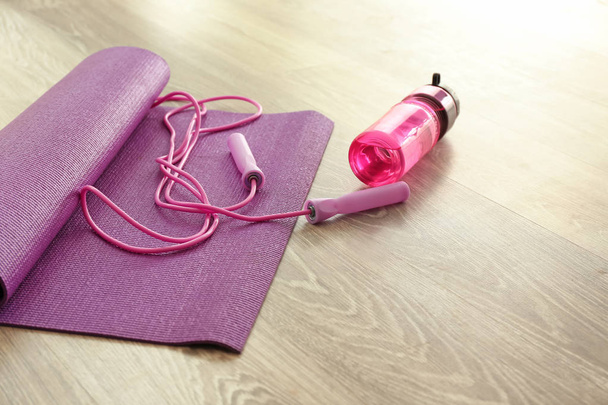 Yoga mat with jumping rope and bottle of water on wooden floor - Photo, image