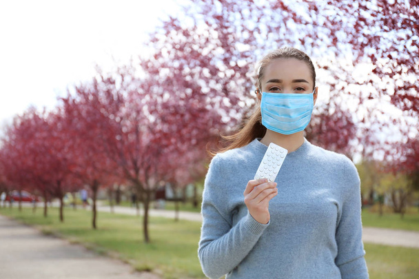 Fiatal nő a gazdaság tabletták közelében virágzó fák védő maszk. Koncepció allergiát - Fotó, kép