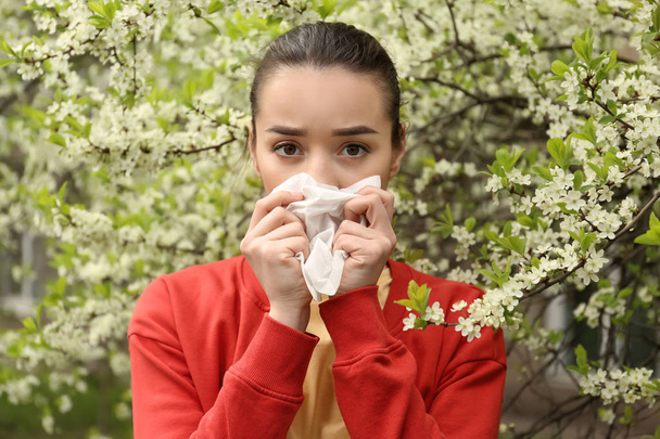 Young woman with nose wiper near blooming tree. Allergy concept - Photo, Image