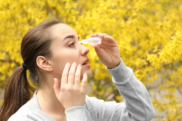 Young woman using eye drops near blooming tree. Allergy concept - Photo, Image