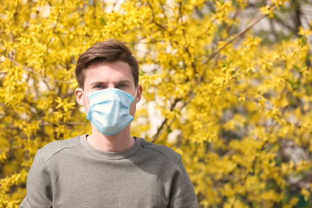 Young man in protective mask near blooming tree. Allergy concept - Photo, Image