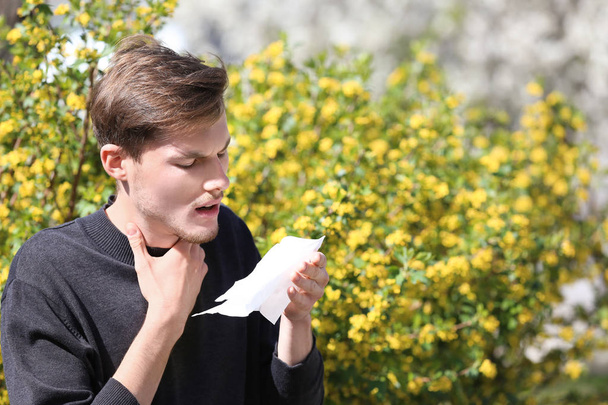 junger Mann mit Nasenwischer in der Nähe eines blühenden Baumes. Allergiekonzept - Foto, Bild