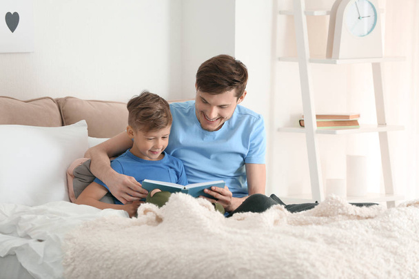 Father and his son reading book together at home - Photo, Image