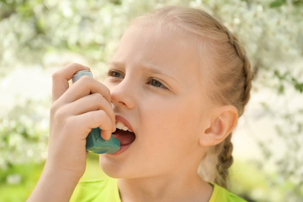 Little girl using inhaler near blooming tree. Allergy concept - Photo, Image