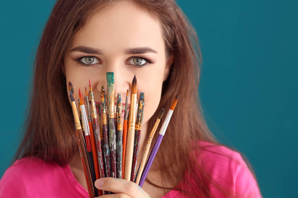 Beautiful female artist with set of brushes on color background - Photo, Image