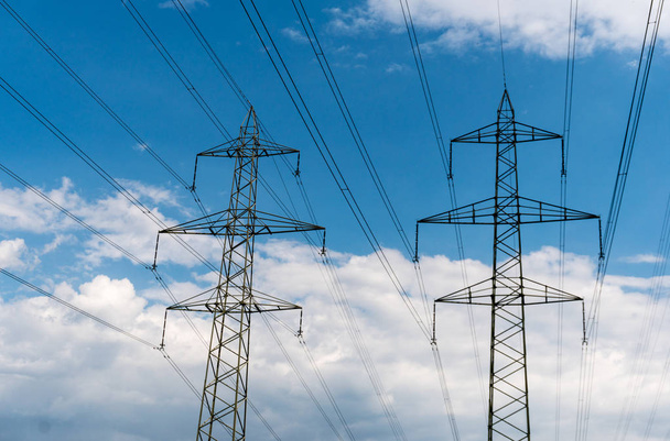 γραμμές ηλεκτρικού ρεύματος και πυλώνες στη Σκιαγραφία ενάντια ένα γαλάζιο ουρανό με άσπρα σύννεφα - Φωτογραφία, εικόνα