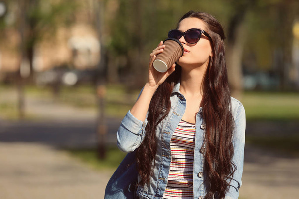 Beautiful young woman drinking coffee while walking in park - Фото, зображення