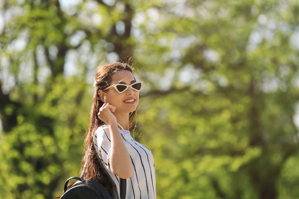 Beautiful young woman listening to music while walking in park - Fotoğraf, Görsel