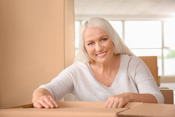 Reife Frau packt Umzugskartons im neuen Zuhause aus - Foto, Bild