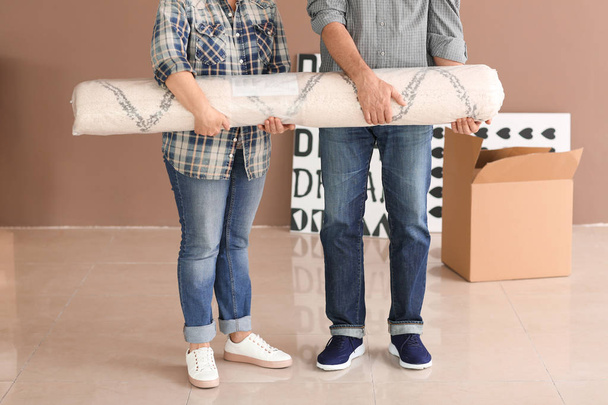 Mature couple carrying carpet in room after moving to new home - Foto, Imagem
