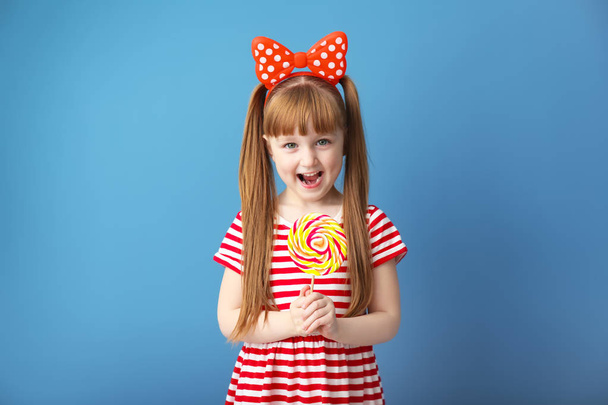 Cute little girl with lollipop on color background - Photo, image