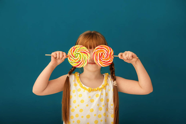 Cute little girl with lollipops on color background - Foto, afbeelding