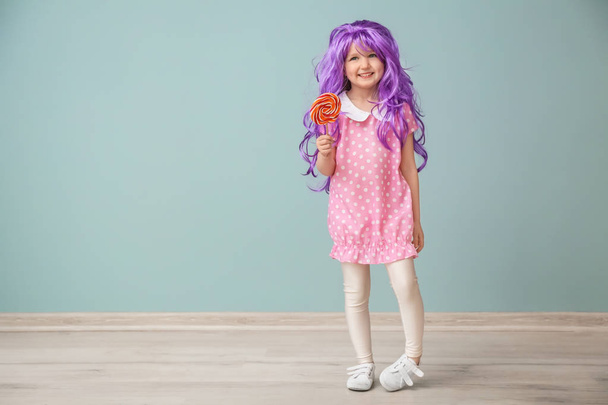 Carino bambina in parrucca viola e con lecca-lecca vicino alla parete di colore
 - Foto, immagini