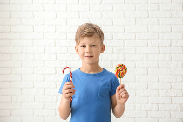 Cute little boy with lollipop and candy cane near white brick wall - Foto, immagini