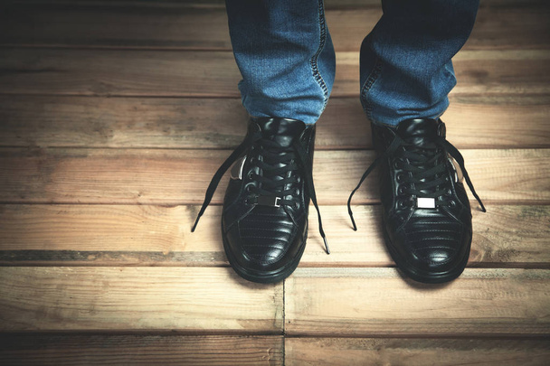 Moda Hombre en zapatilla de deporte negro con vaqueros azules en el fondo del piso de madera
. - Foto, imagen