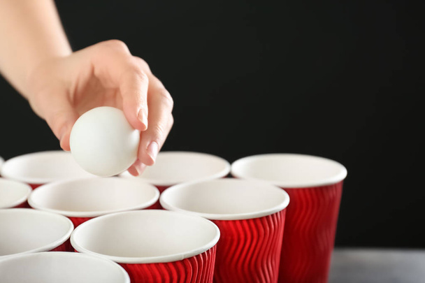 Femme tenant boule blanche sur des tasses disposées pour jouer au bière pong, gros plan
 - Photo, image
