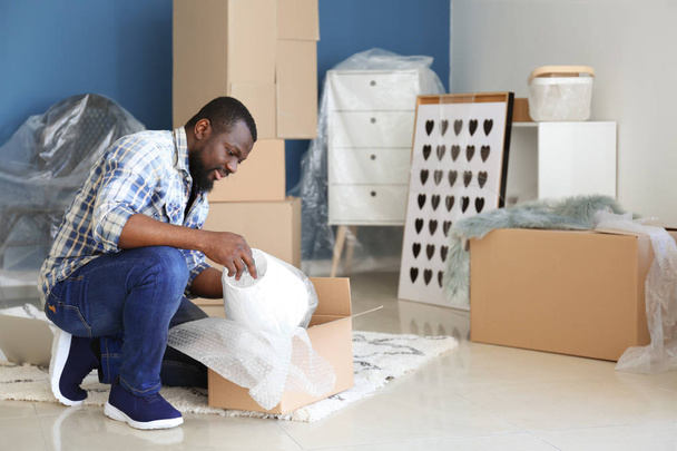 Αφρικανικός-Αμερικανός άνθρωπος αποσυσκευασία πλαίσιο σε εσωτερικούς χώρους. Μετακίνηση σε νέο σπίτι - Φωτογραφία, εικόνα