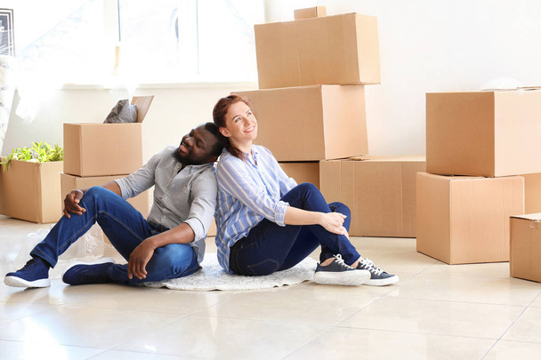 Interracial couple sitting on floor near boxes. Moving into new house - Photo, Image