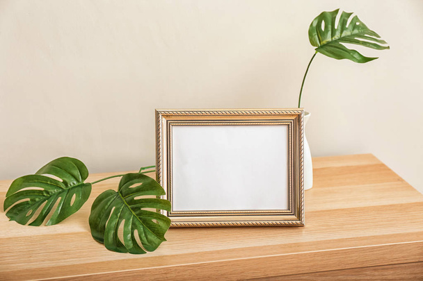 Photo frame with vase and green leaves on table near light wall - Photo, Image