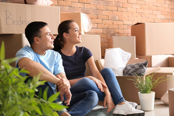 Young couple resting near boxes indoors. Moving into new house - Photo, Image