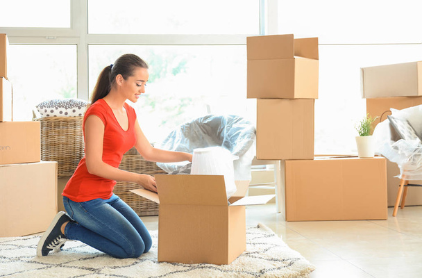 Young woman unpacking box indoors. Moving into new house - Photo, Image