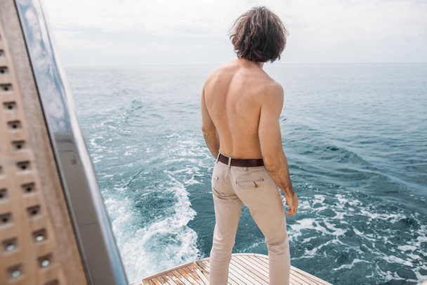 Rear view of young man sitting at edge of yacht looking at sea - Фото, зображення