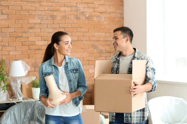 Young couple with box and vase indoors. Moving into new house - Photo, Image