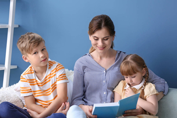 Mother and her children reading book together at home - Foto, Bild