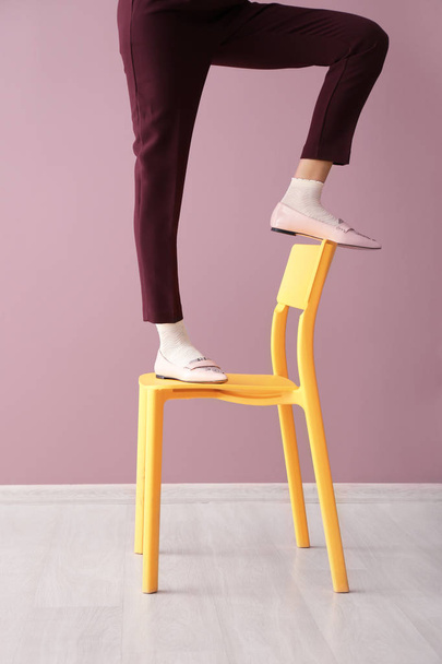 Jambes de belle jeune femme debout sur la chaise contre le mur de couleur
 - Photo, image