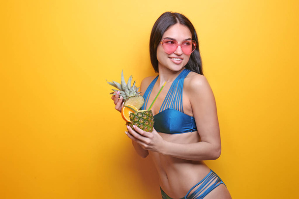 Hermosa mujer joven en bikini con bebida y gafas de sol sobre fondo de color
 - Foto, Imagen