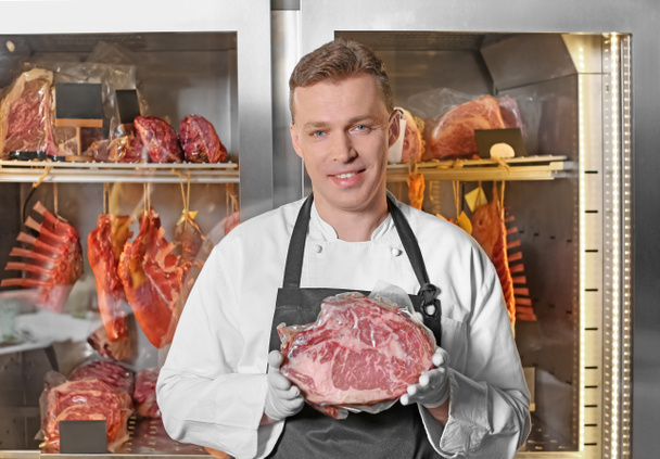 Jeune homme tenant un morceau de viande crue dans une boucherie
 - Photo, image
