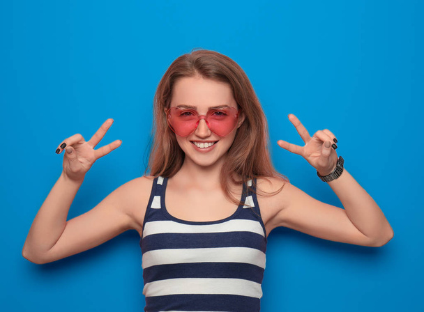 Schöne junge Frau zeigt Siegesgeste auf farbigem Hintergrund - Foto, Bild