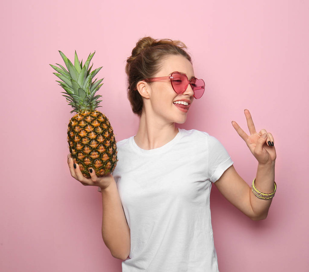 Portrait of beautiful young woman with pineapple showing Victory gesture on color background - Photo, Image