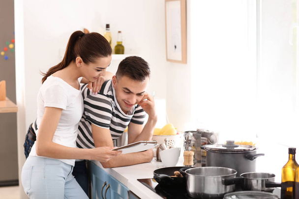 Young couple reading recipe book in kitchen - Foto, afbeelding