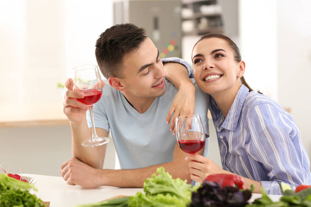Nuori pari juo viiniä keittäessään yhdessä keittiössä
 - Valokuva, kuva