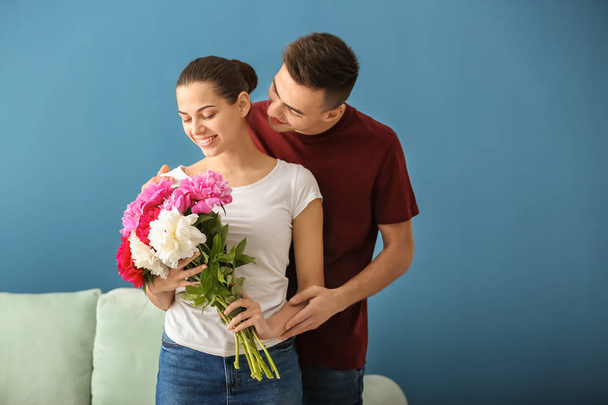 Young woman with beautiful flowers and her beloved boyfriend indoors - Photo, Image