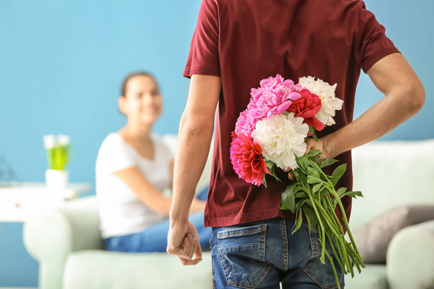 Jeune homme cachant des fleurs pour petite amie derrière son dos à l'intérieur
 - Photo, image