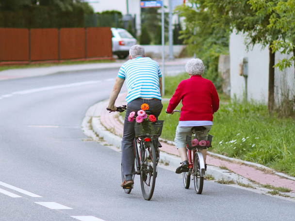 Homem e mulher maduros monta uma bicicleta entre os verdes. Uma parte saudável e ativa da vida. Transporte ecológico para a população. Tempo livre para a reforma. Movimento no espaço. Esportes para os mais velhos
 - Foto, Imagem