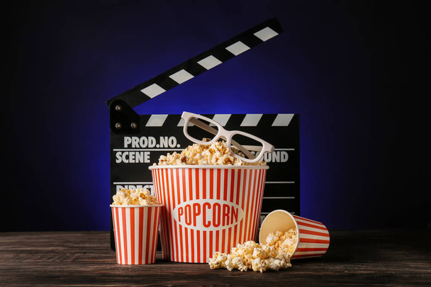 Cups with tasty popcorn, glasses and clapperboard on dark background - Photo, Image
