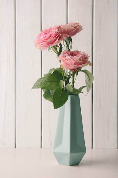 Vase with bouquet of beautiful roses on table against wooden background - Foto, immagini