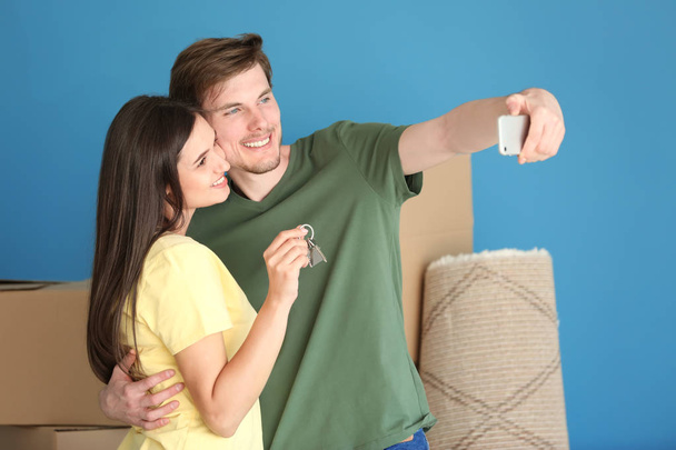 Νεαρό ζευγάρι ευτυχισμένο λαμβάνοντας αυτοπορτρέτα με κλειδί του νέου σπιτιού τους σε εσωτερικούς χώρους - Φωτογραφία, εικόνα