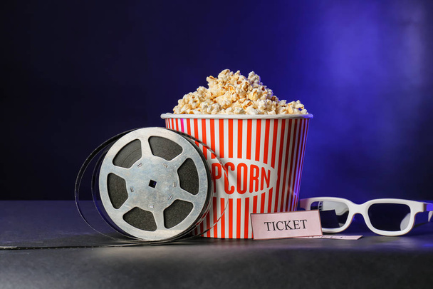 Emmer met lekkere popcorn en een film reel op donkere achtergrond - Foto, afbeelding