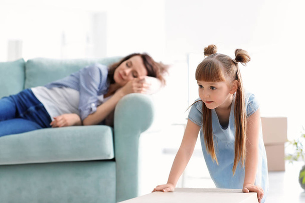 Nettes Mädchen mit Pappschachtel und ihrer Mutter, die auf dem Sofa ruht. Umzug in neues Haus - Foto, Bild